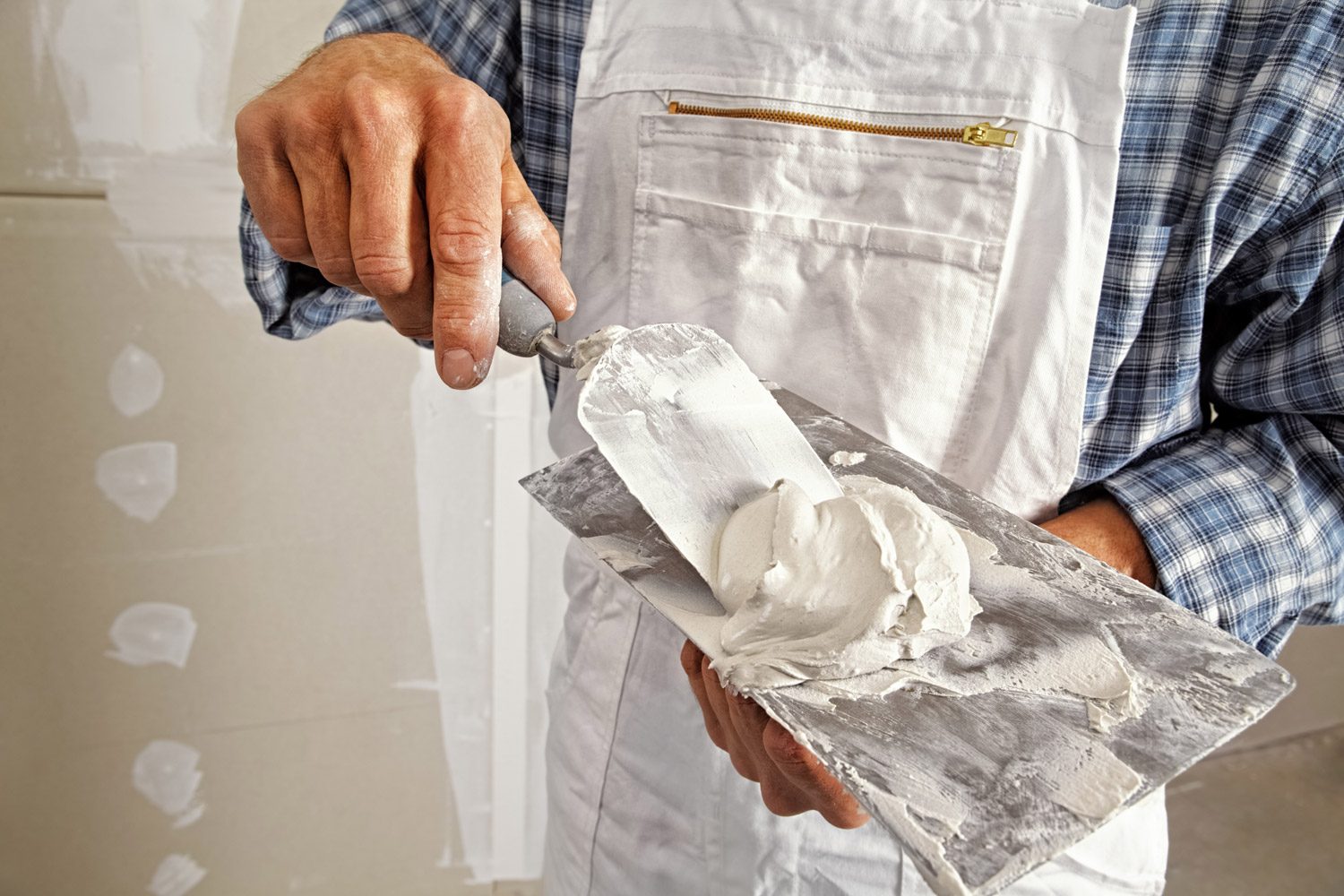 Zdjęcie przedstawiające fachowca precyzyjnie nakładającego masę szpachlową na ścianę, co ukazuje profesjonalizm i dbałość o detale.